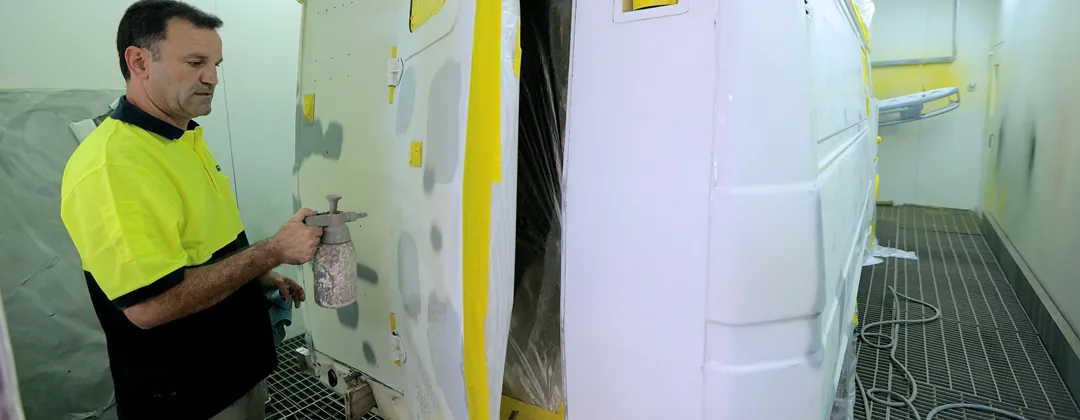 A Pro Paint 'n Panel spray painter working on a masked-up van inside the booth.